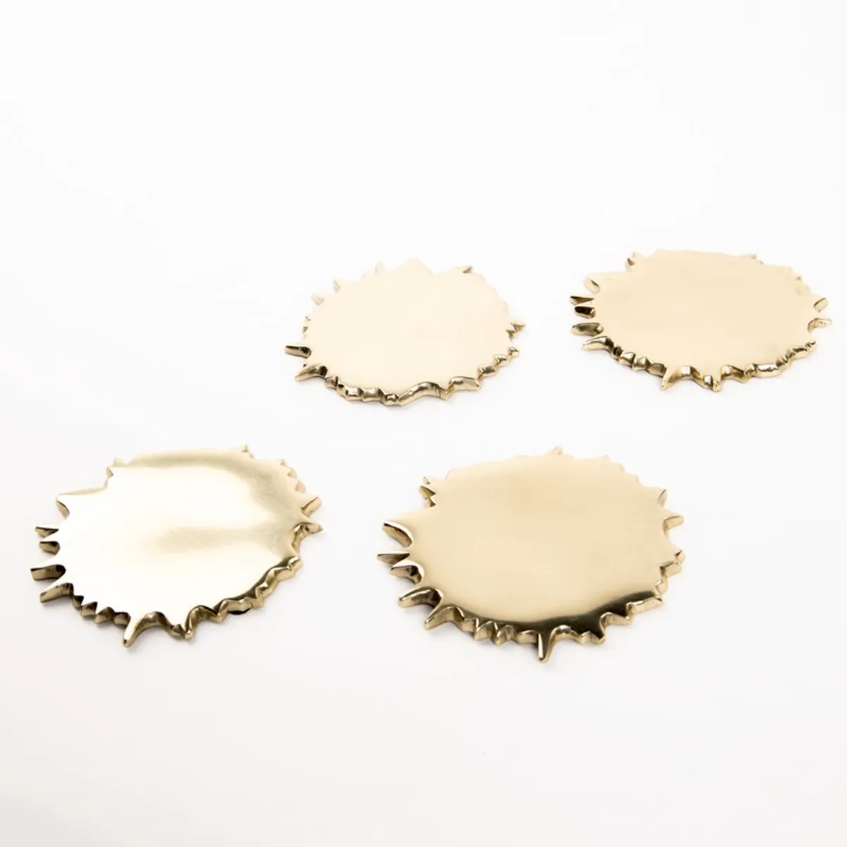 Set of four gold spill-shaped coasters on a white background