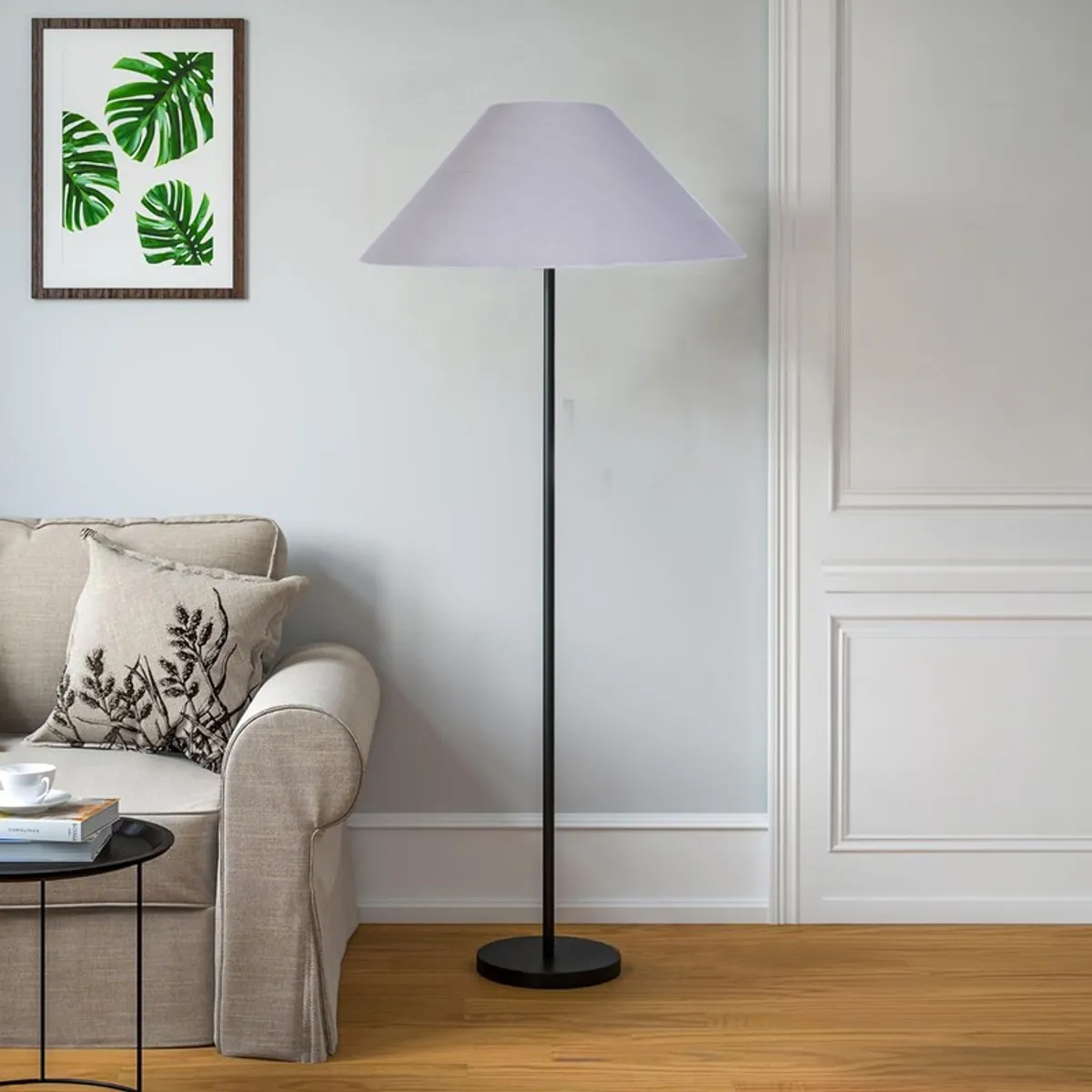 Floor lamp with pale grey cone shade placed beside a sofa in a bright living room