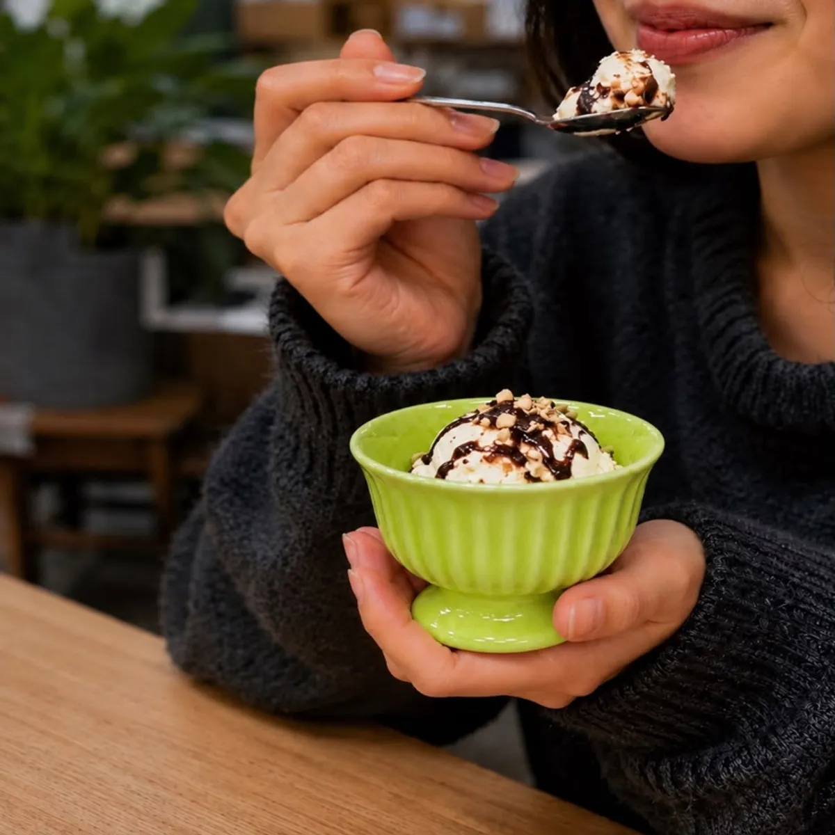 Person holding a green pedestal ice cream cup filled with dessert