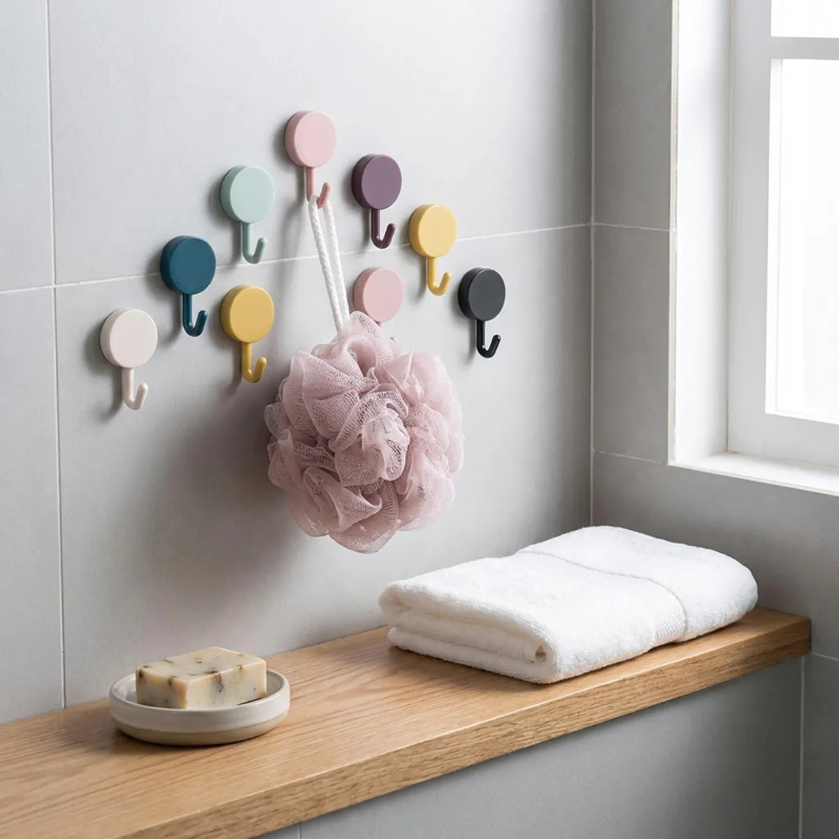 Multicolour adhesive hooks on a tiled wall holding a bath sponge and cloth.