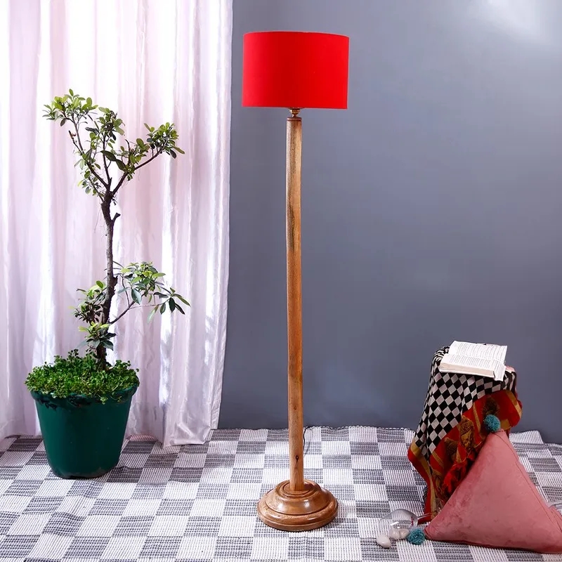 Wooden floor lamp with red drum shade in a room setting beside a potted plant