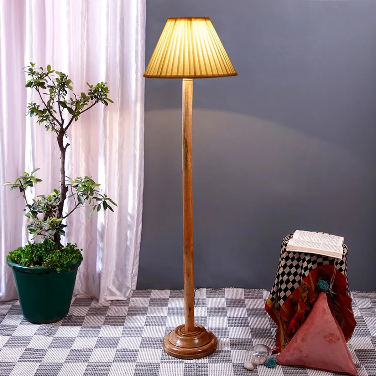 Wooden floor lamp with warm lit pleated shade in a styled indoor setting