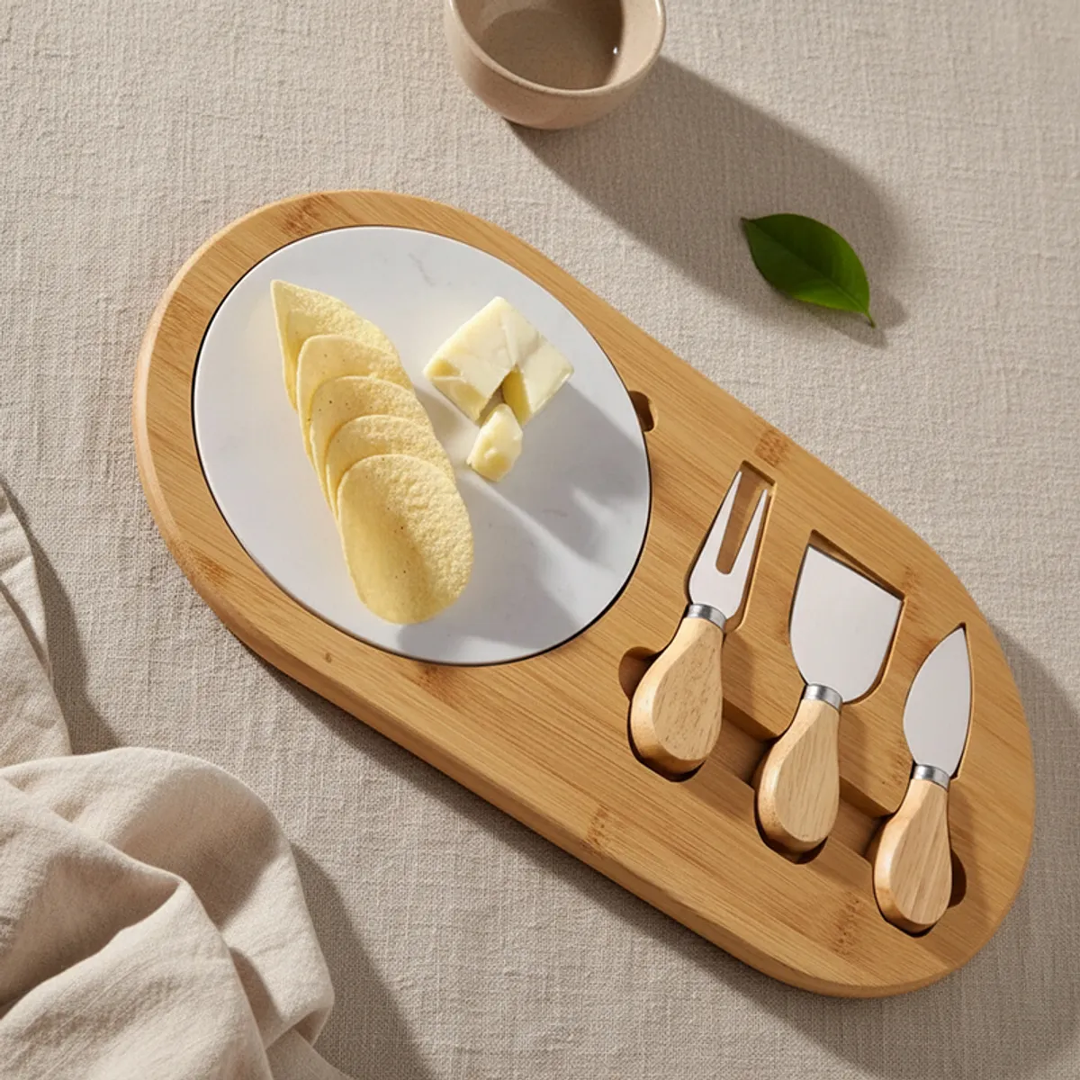 Wooden cheese platter styled on fabric with marble centre and three cheese tools