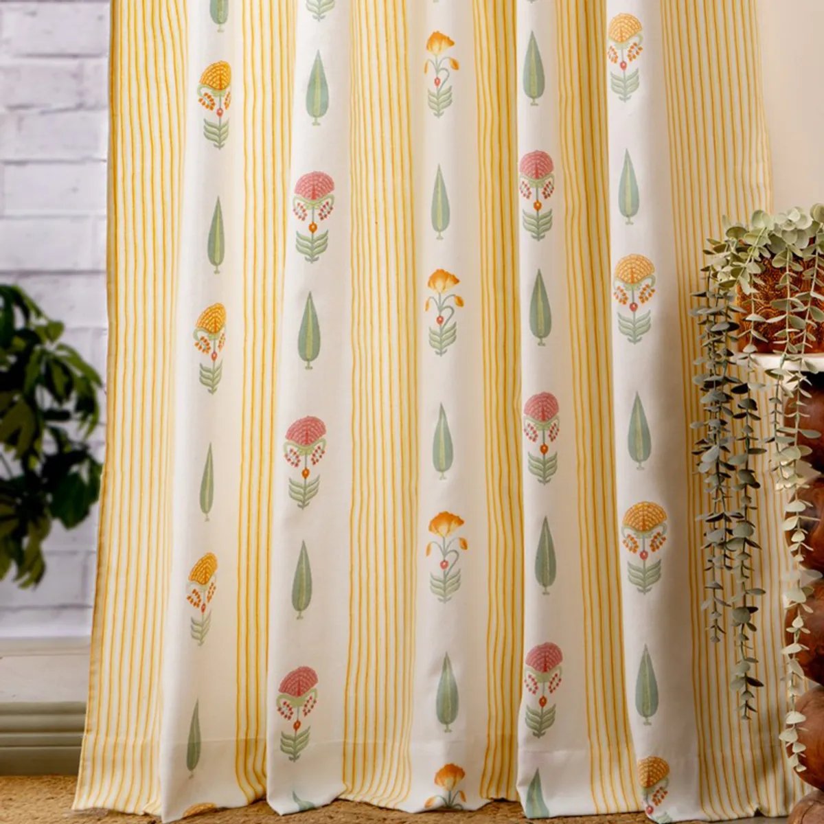 Patterned yellow curtains styled beside a potted plant and white brick wall