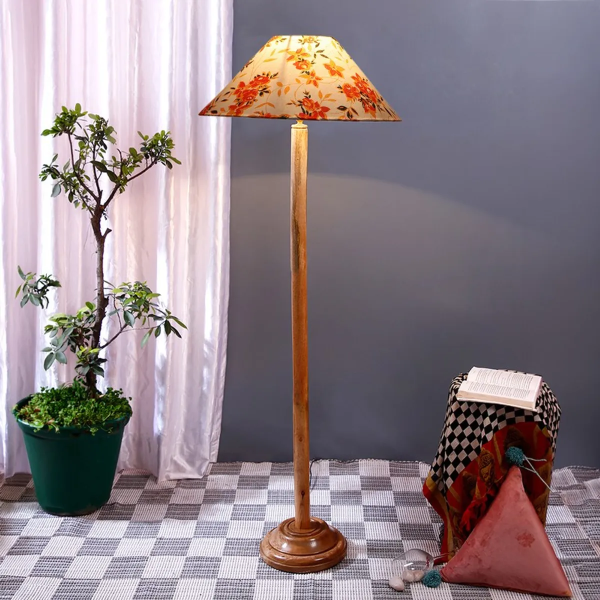 Wooden floor lamp with a floral cotton shade styled against a grey wall with a plant nearby.