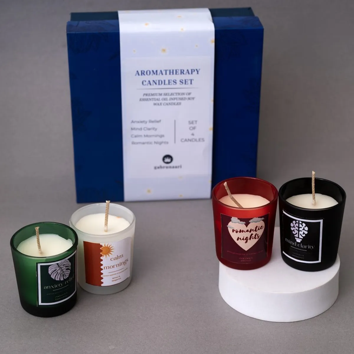 Four unlit jar candles arranged in front of a blue gift box on a grey surface.