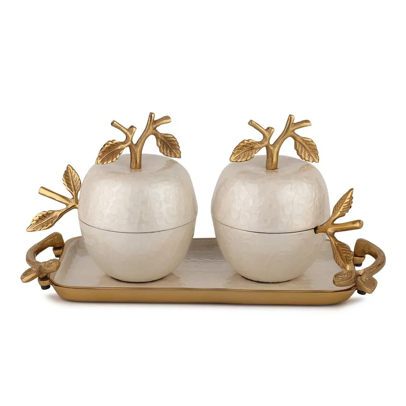 Two ivory jars with sculpted gold apple lids on a rectangular tray