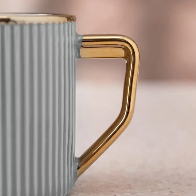 Side close-up of the gold-toned angular handle on a grey ribbed mug