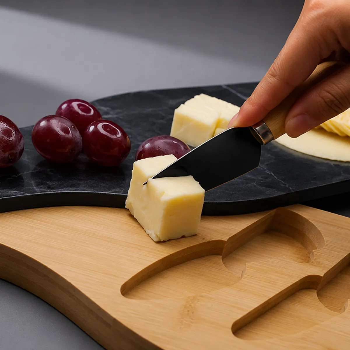 Close-up of cheese being cut on a black marble board over a wooden base