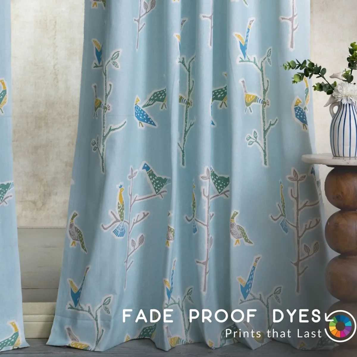 Light blue curtain with colourful bird-and-branch pattern beside a vase