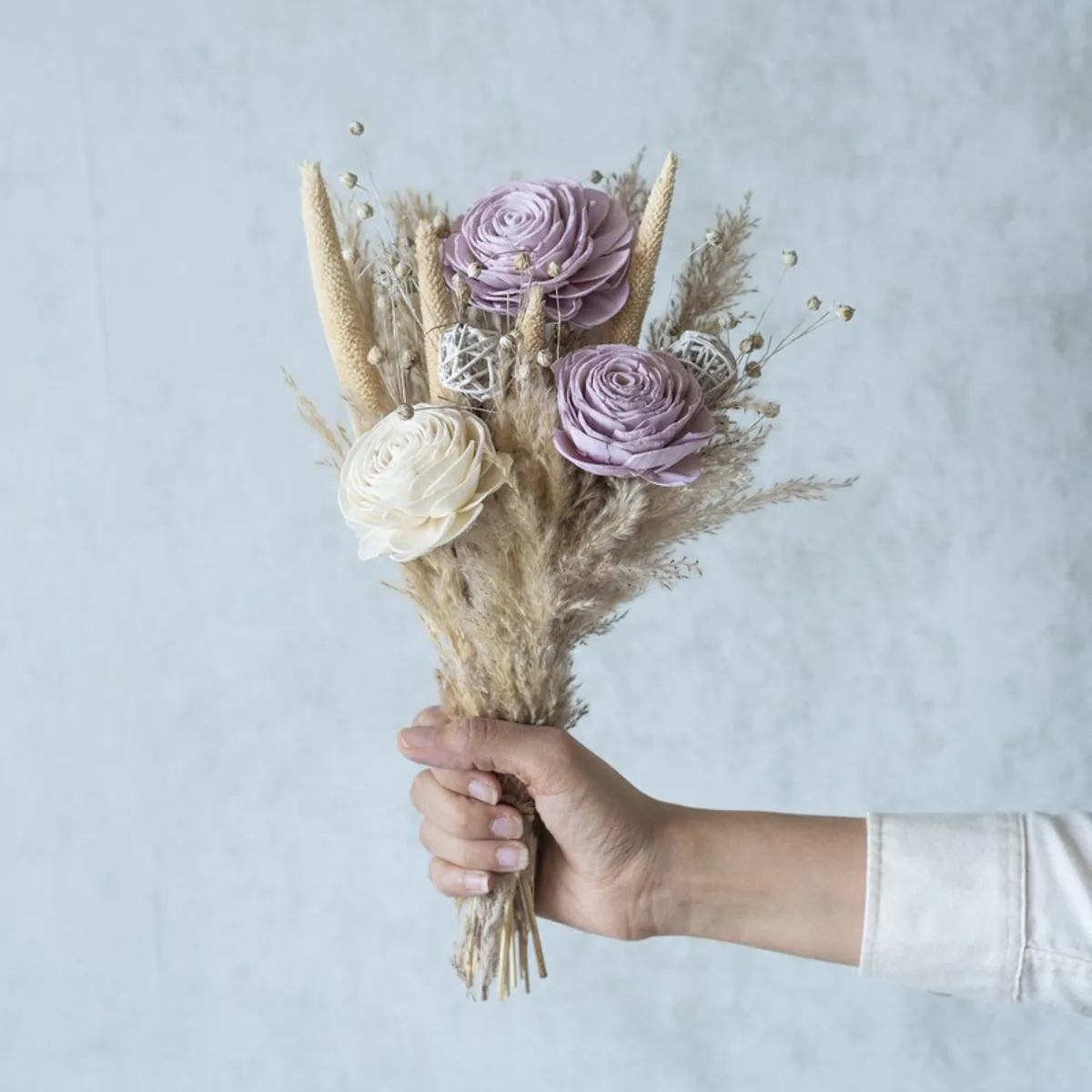 Handheld view of a beige, white and purple dried flower bunch.