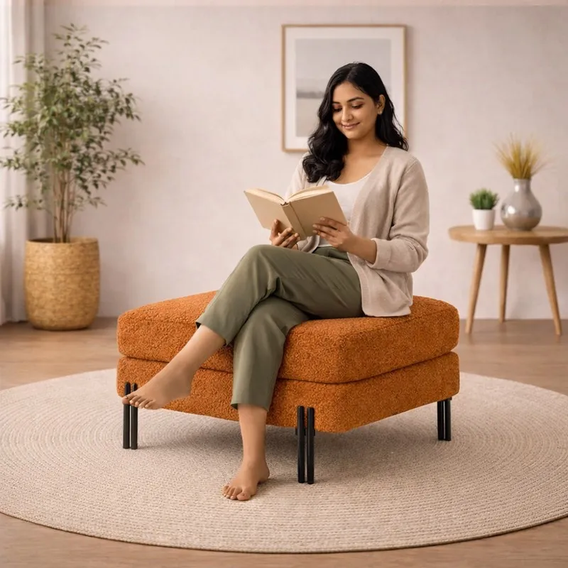 Person seated on a rust bouclé ottoman with black legs while reading