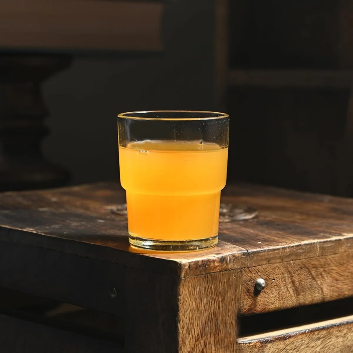 Single clear glass filled with orange juice on a rustic wooden table