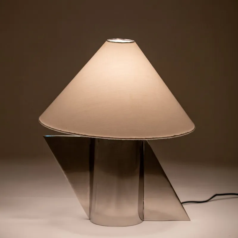 Lit table lamp with white shade and reflective silver geometric base