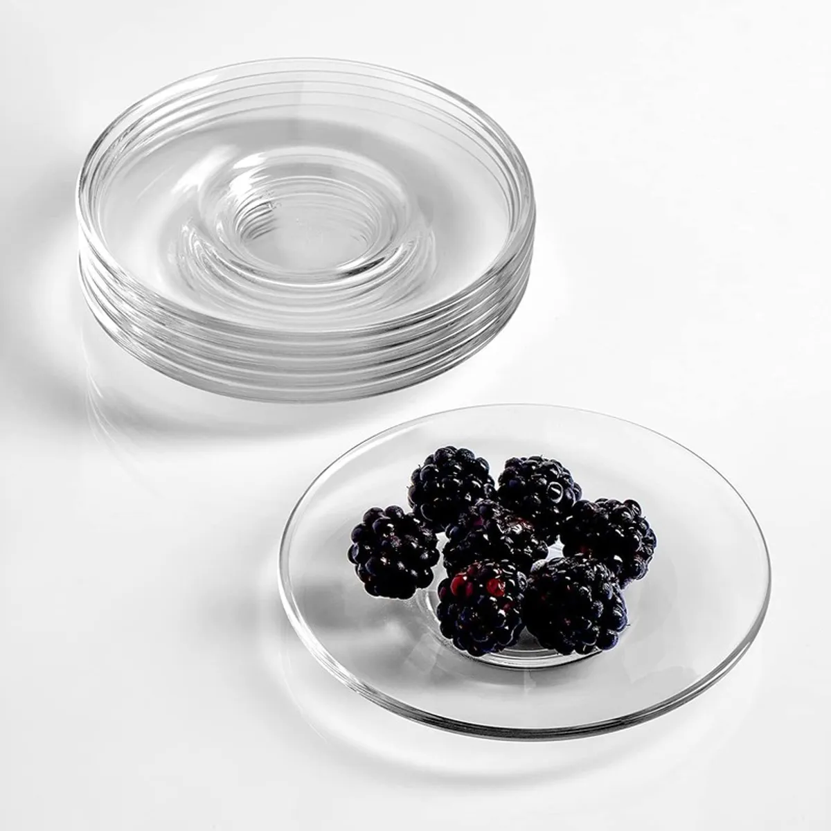 Stacked transparent glass saucers beside one saucer with blackberries