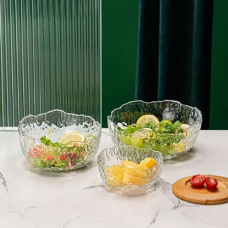 Three transparent glass bowls with textured surfaces arranged with salad and fruit
