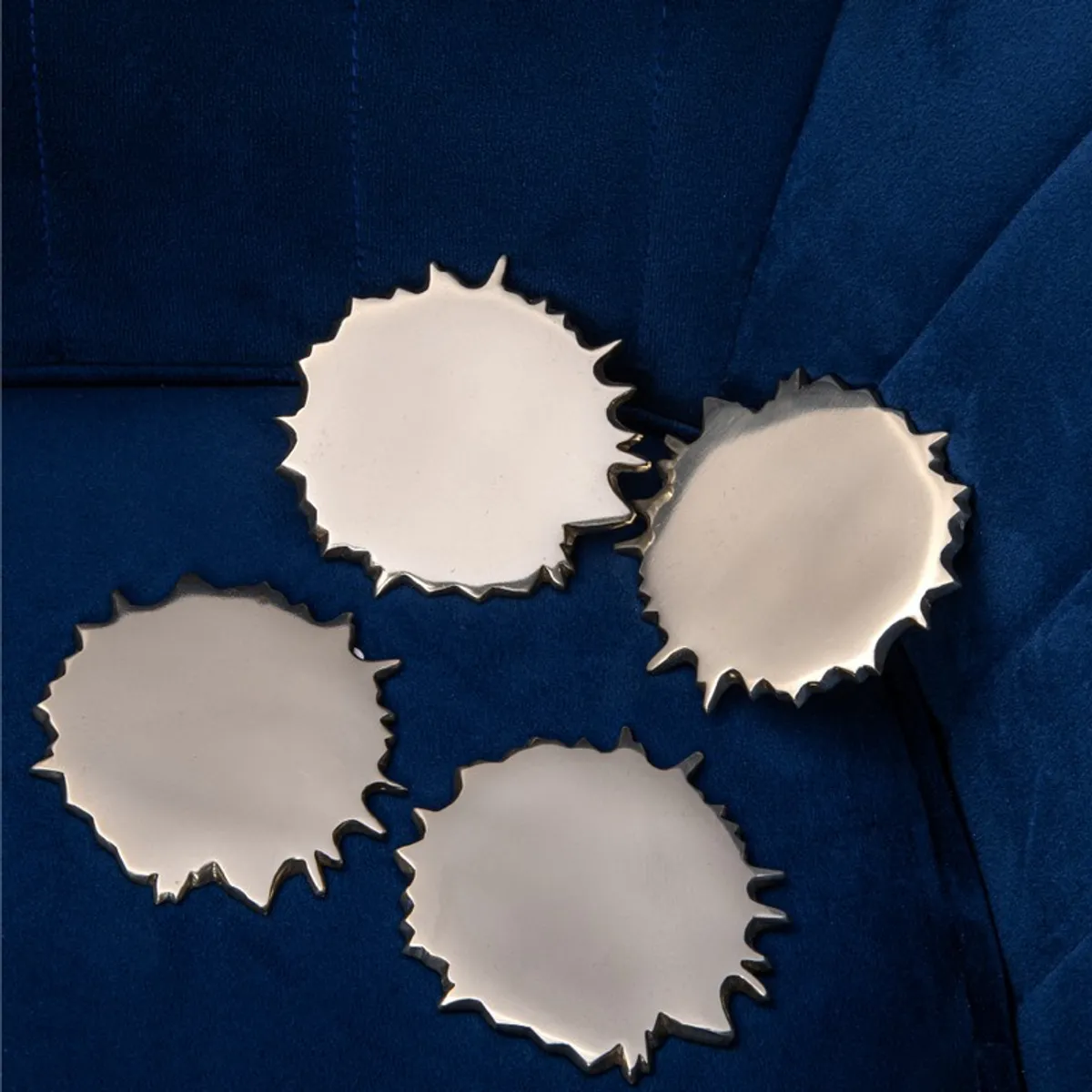 Set of four gold spill-shaped coasters placed on a blue upholstered chair