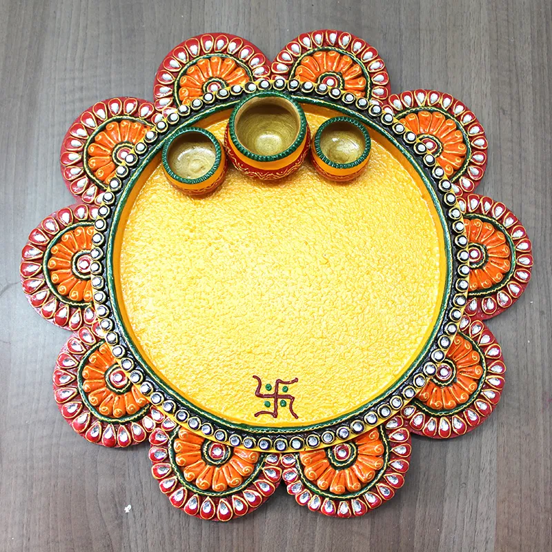 Yellow round pooja thali with ornate floral rim and three bowls on a wooden surface