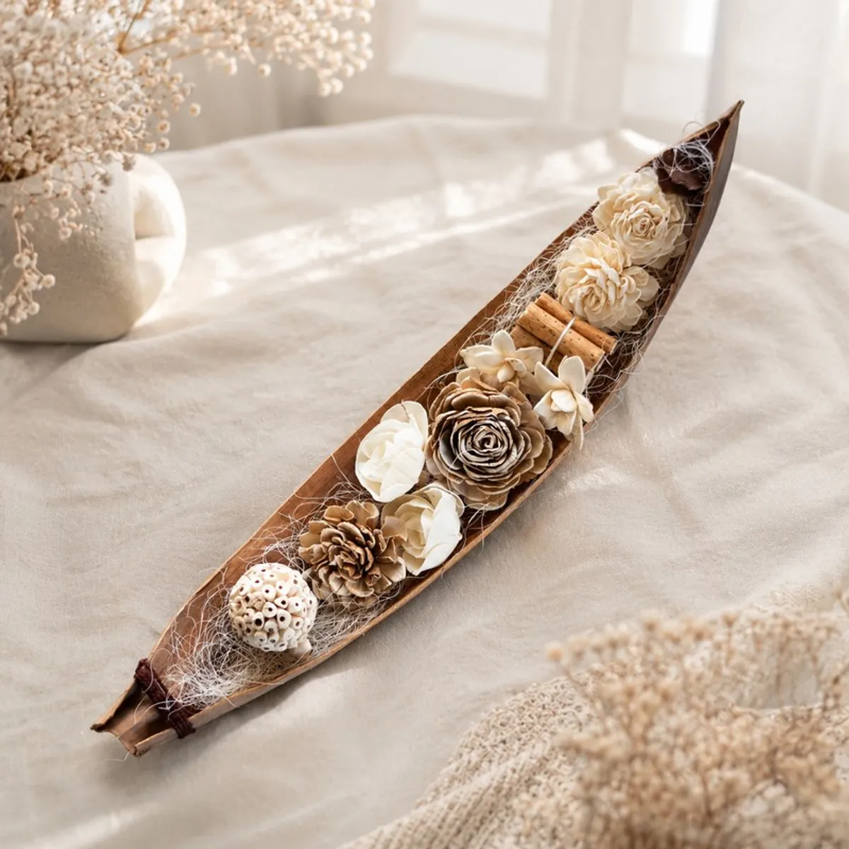 Elongated floral arrangement with cream and brown flowers styled on a light table