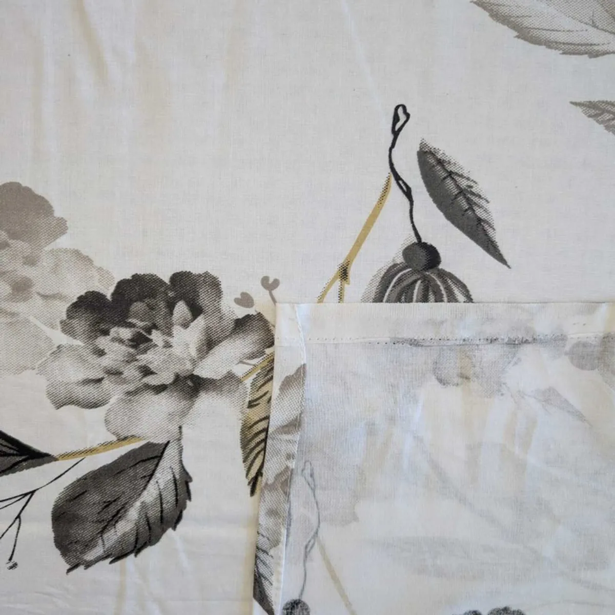 Close-up of floral print and stitched edge on white bedsheet fabric