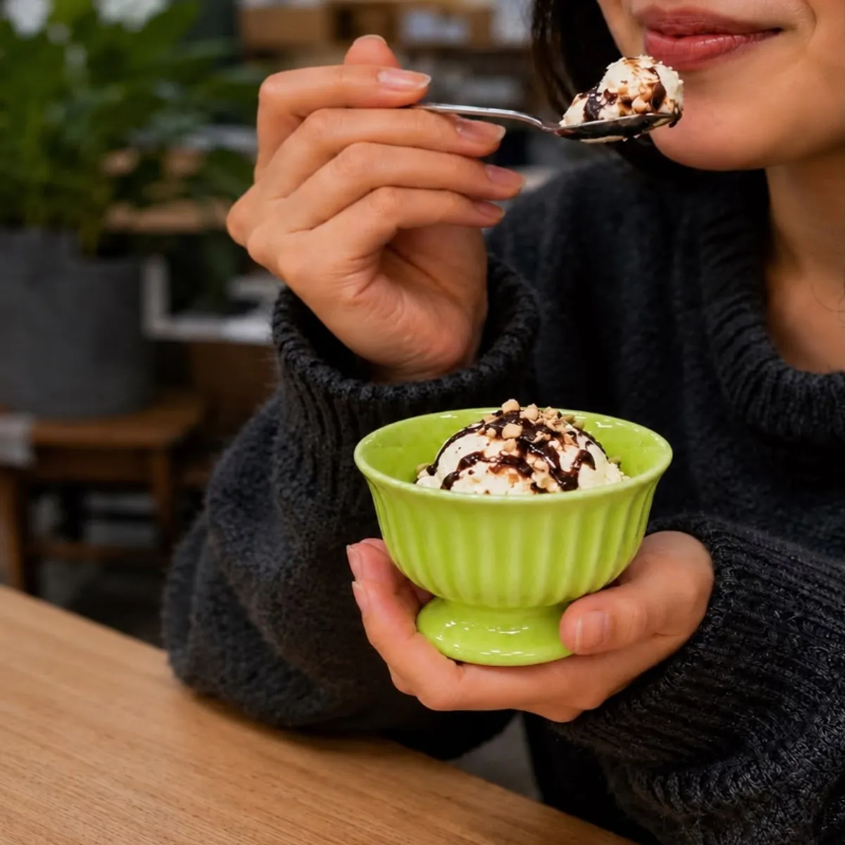 Person holding a green ceramic dessert cup filled with ice cream.