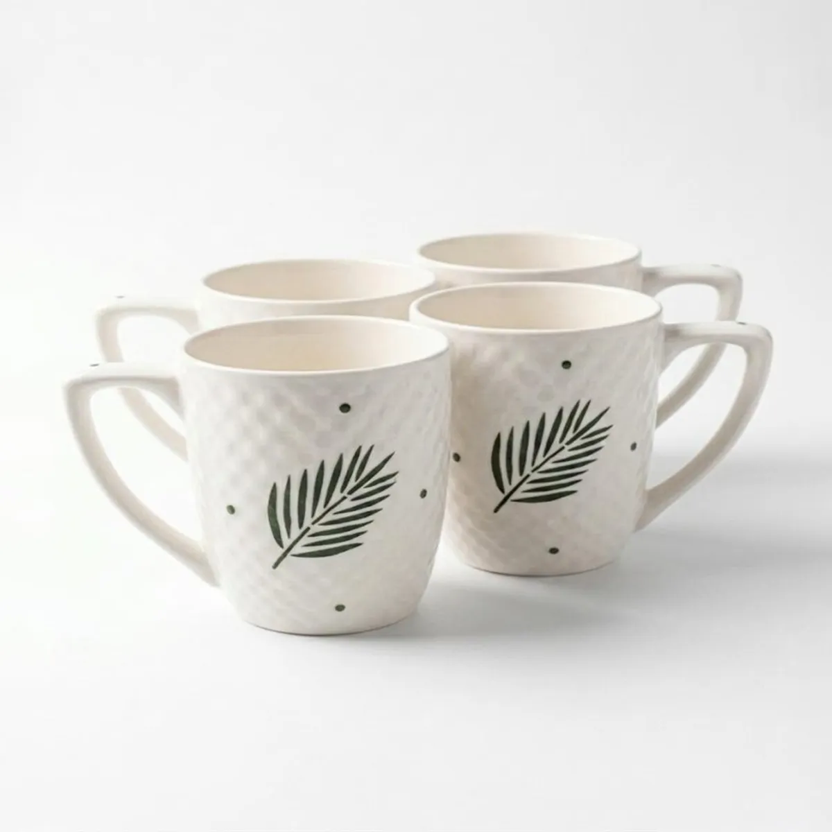 Four white mugs with green leaf motifs grouped against a white background