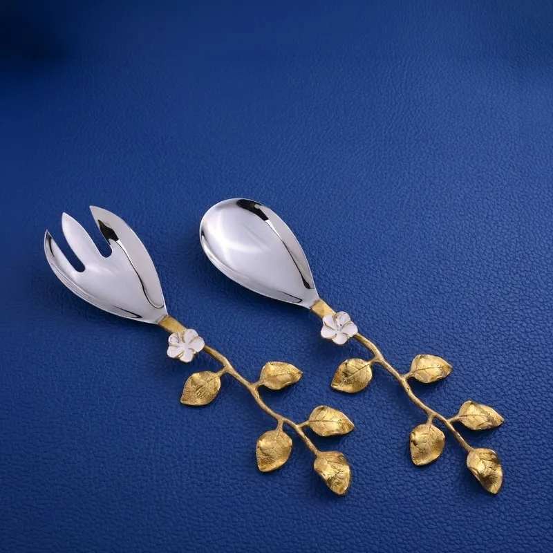 Silver and gold leaf salad spoon and fork displayed on a blue surface