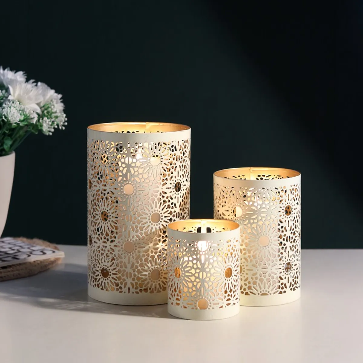 Three white perforated floral candle holders casting warm light against a dark background
