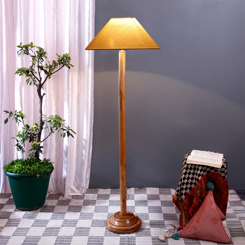Wooden floor lamp with a warm beige cone shade beside a potted plant and draped stool.
