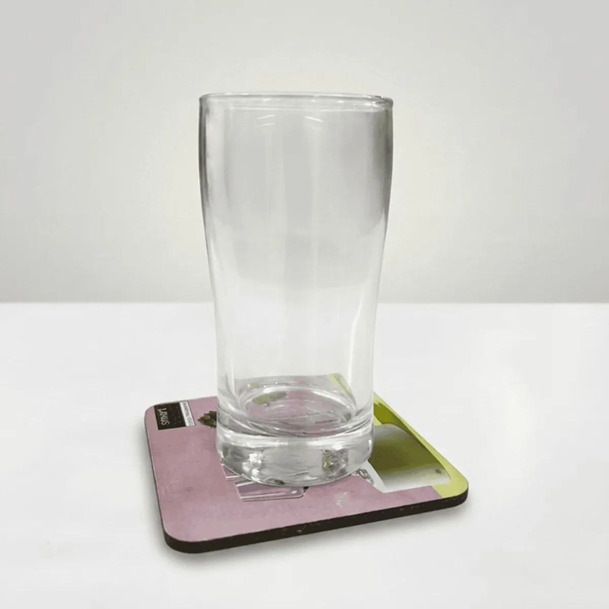 Single clear cylindrical drinking glass shown on a square coaster