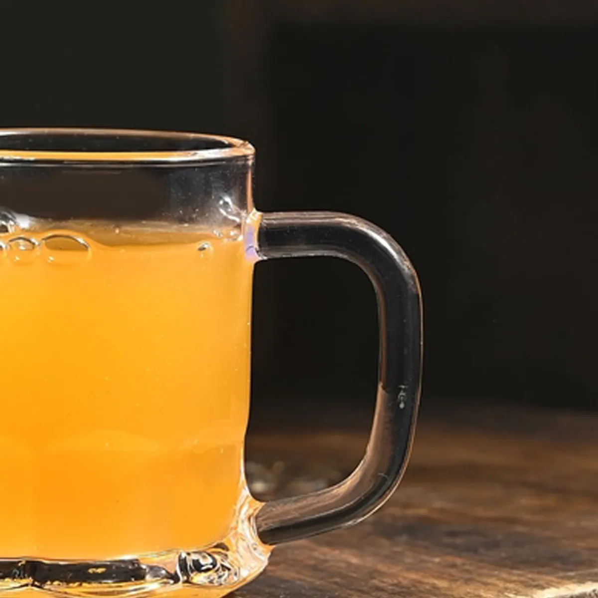 Close-up of a transparent glass mug handle beside a warm orange beverage.