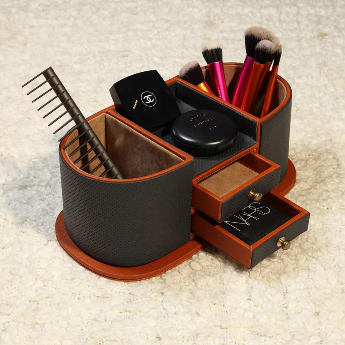 Grey and brown desk organiser holding makeup brushes and accessories on a light textured surface