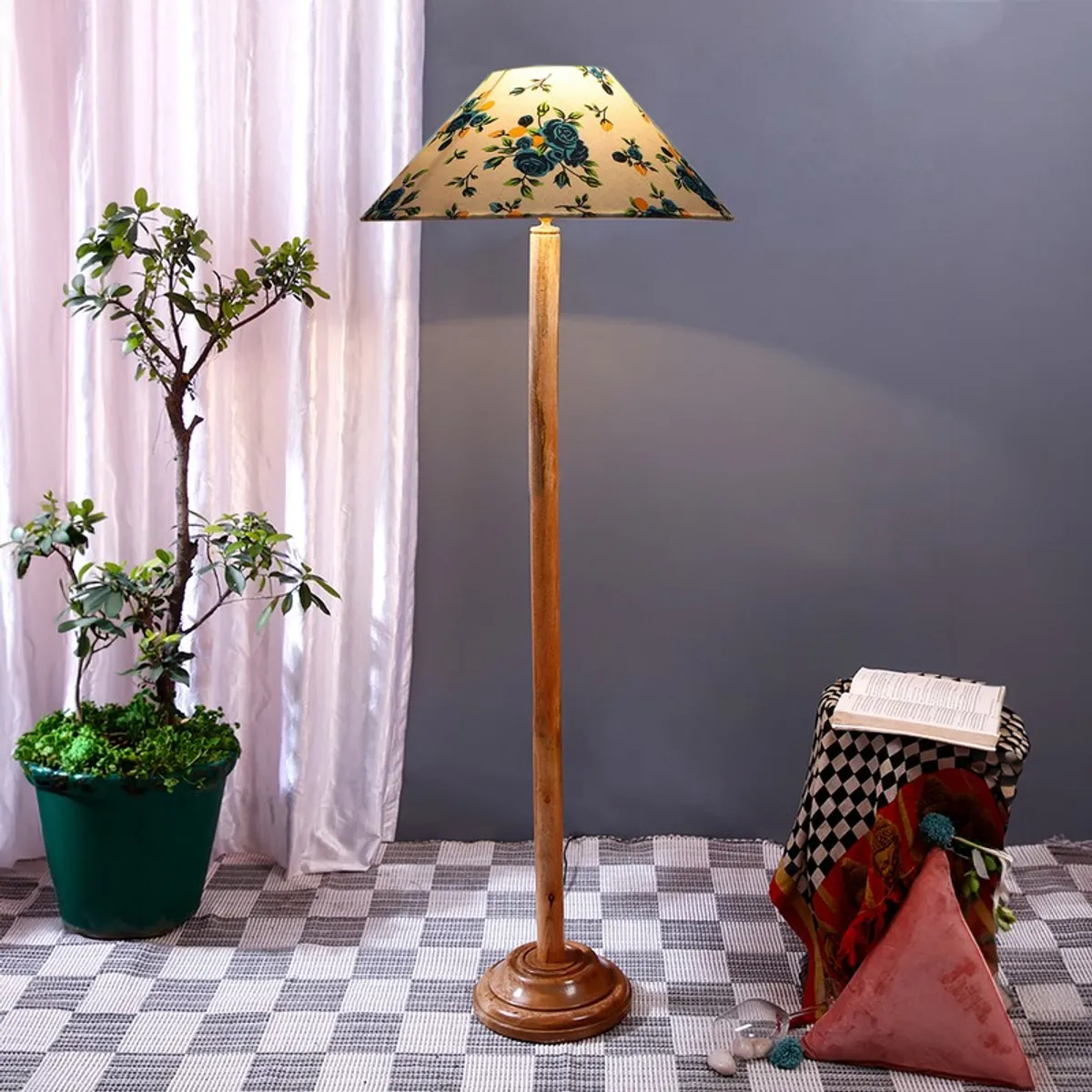 Blue floral floor lamp with wooden stand in a room setting with curtains and potted plant