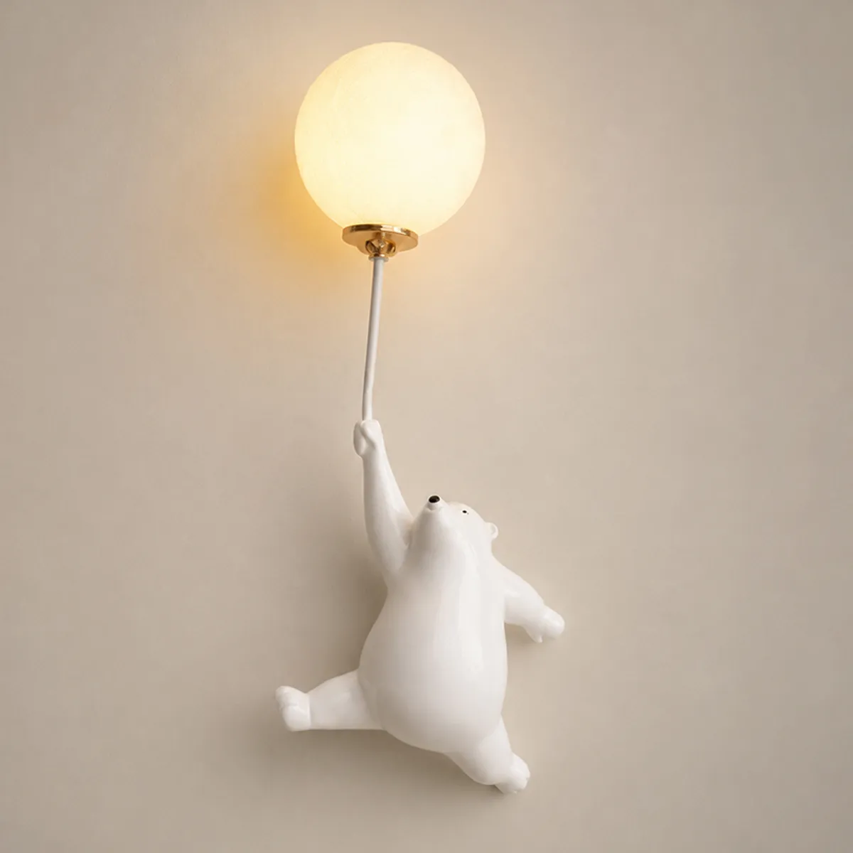 Close-up of white bear wall lamp holding a lit round globe