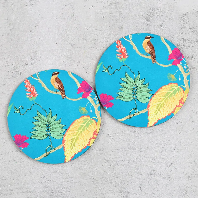 Two round blue coasters featuring tropical birds, leaves and flowers