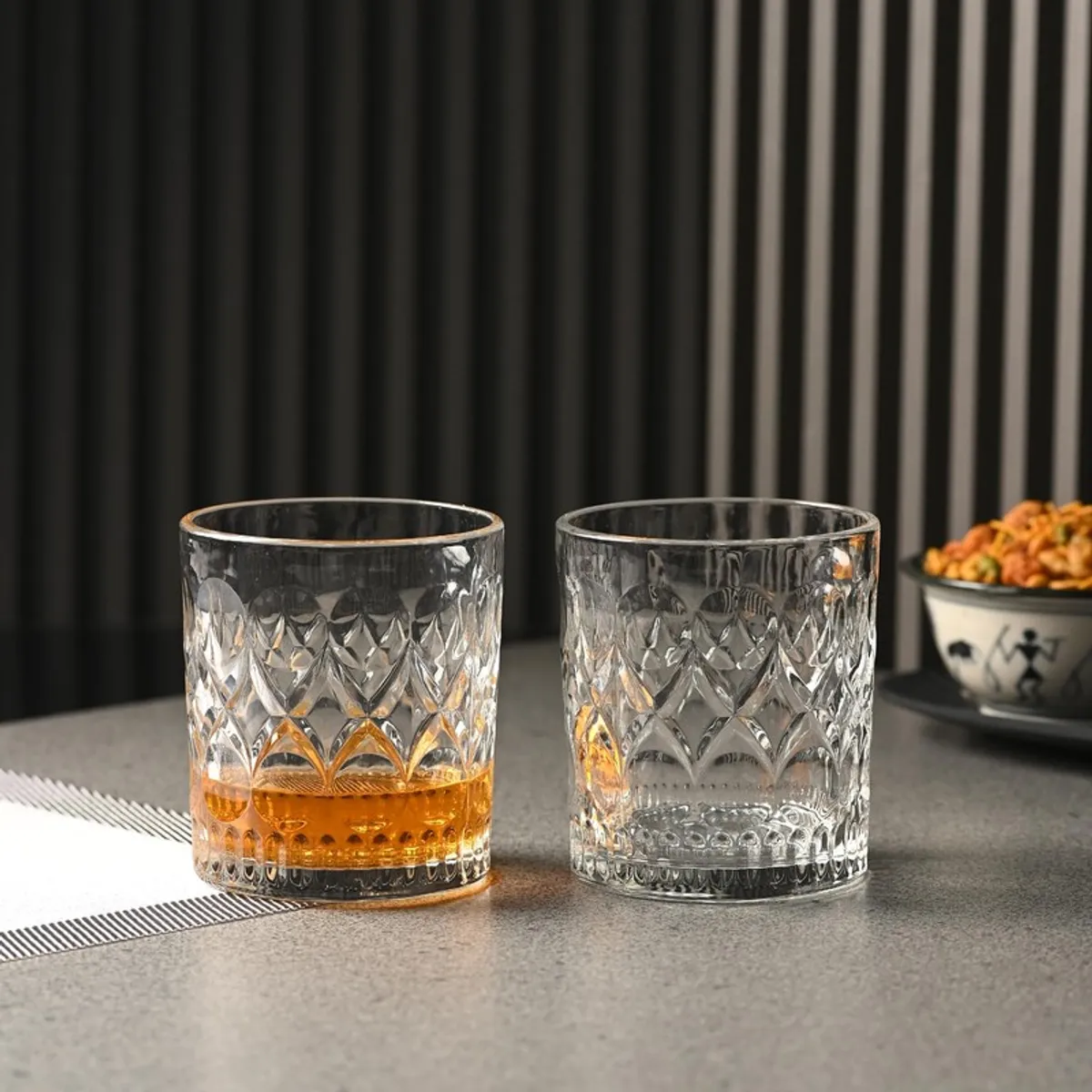Two clear geometric-pattern whiskey glasses with amber whiskey on a dining table