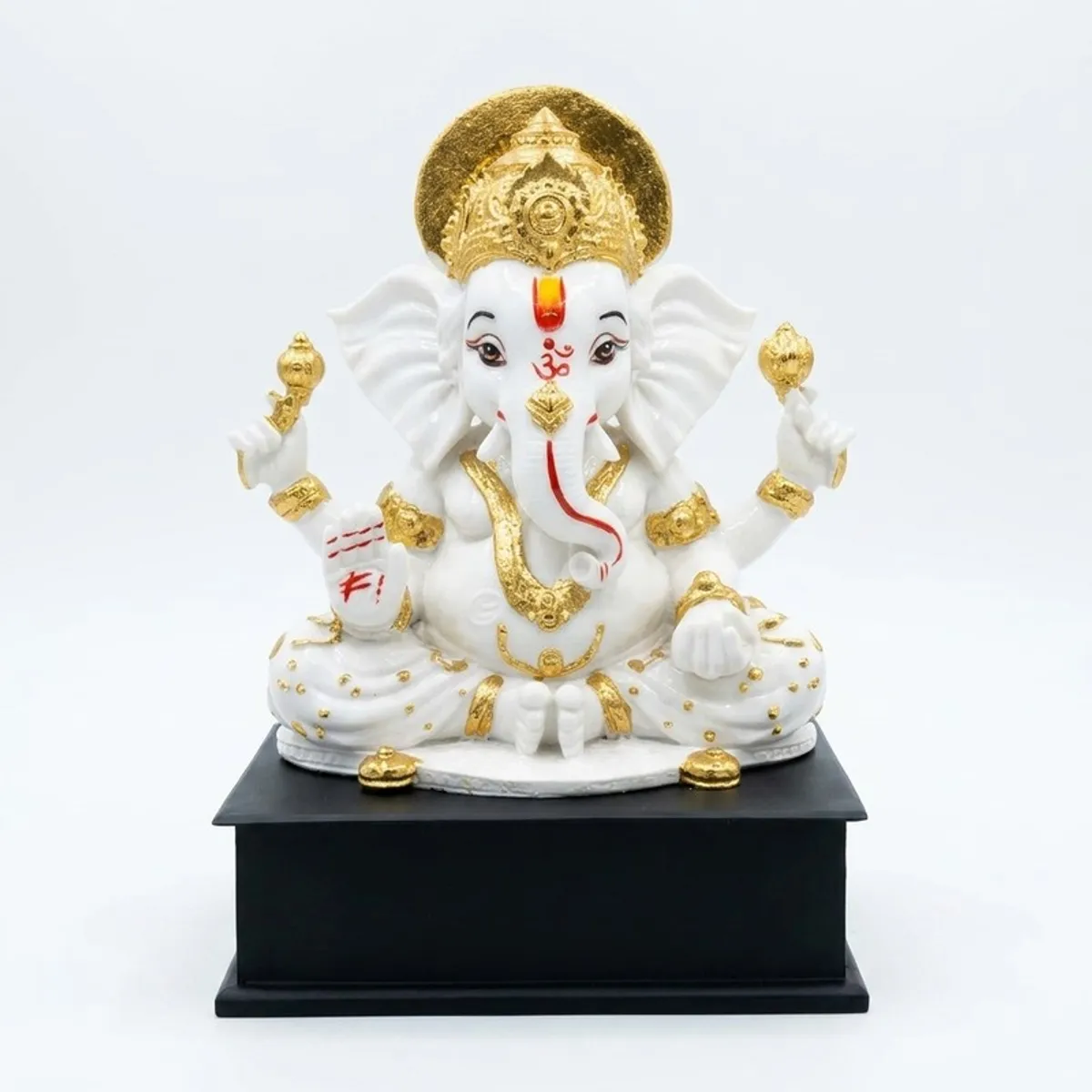 Front view of a white and gold Ganesha idol on a black pedestal