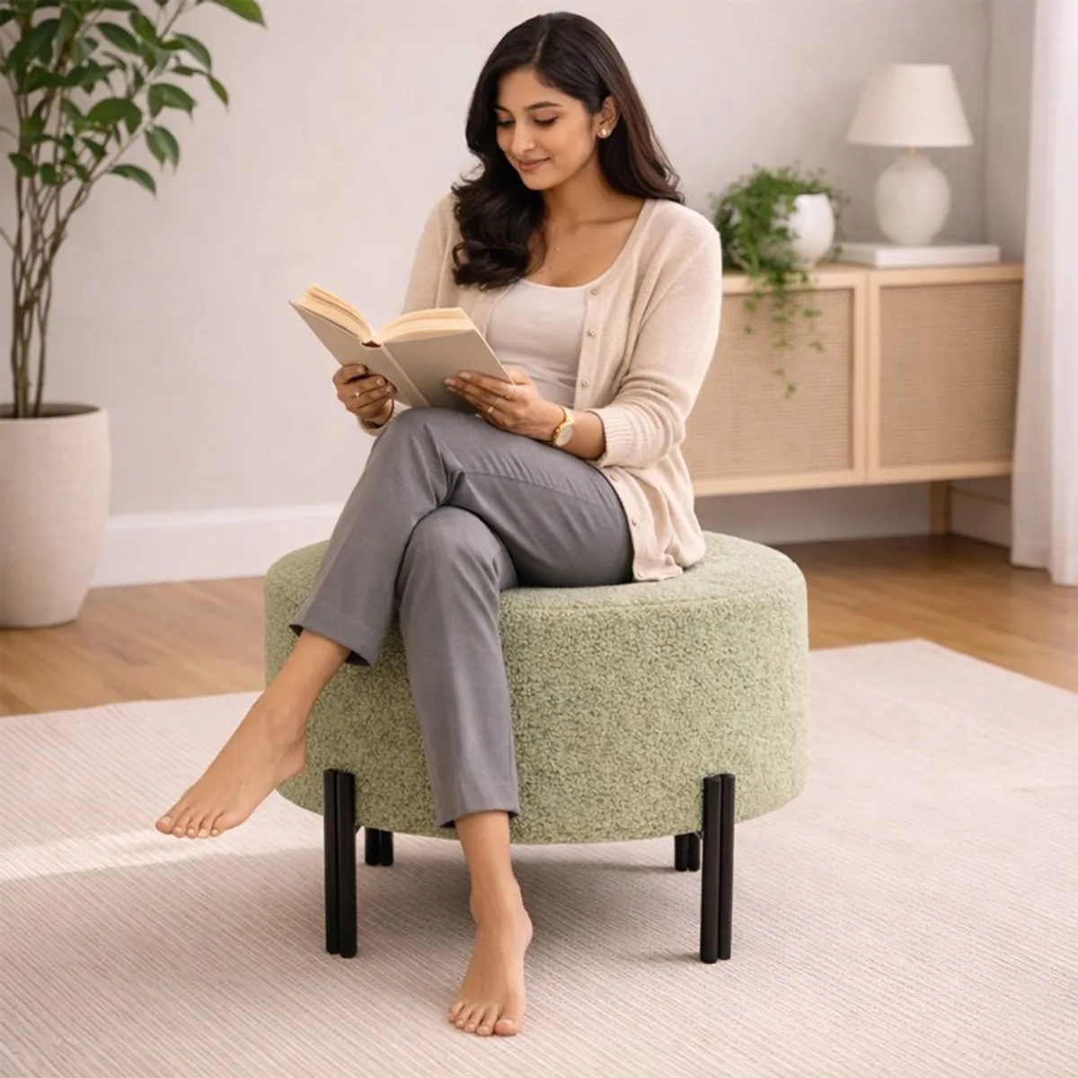 Woman seated on a sage green round ottoman with black legs