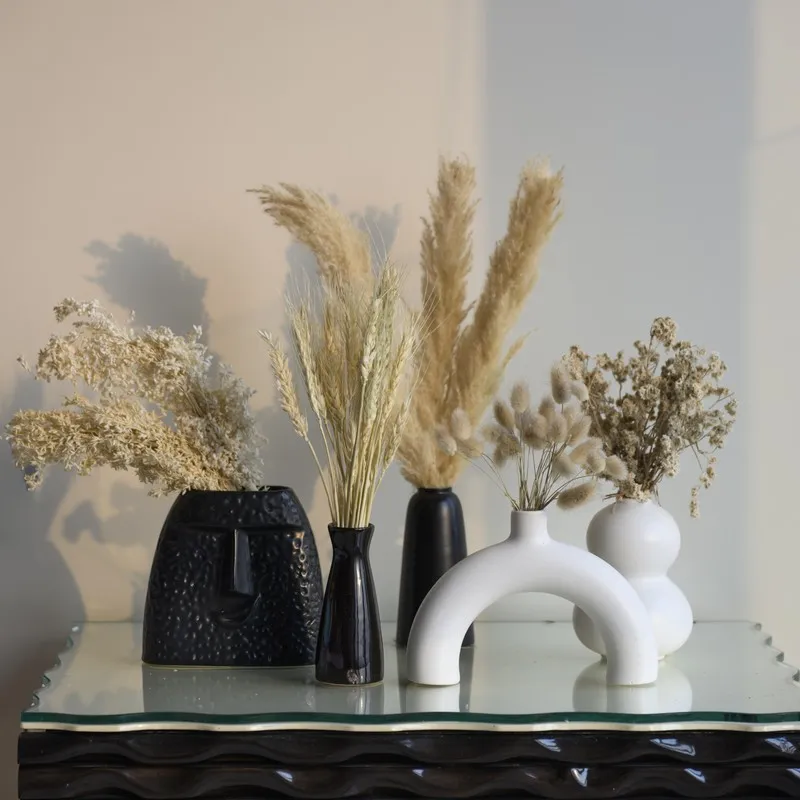 Beige dried flowers styled in black and white vases on a decorative table.