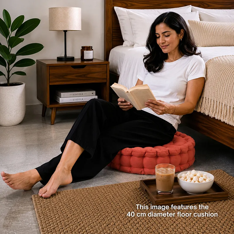 Woman reading while seated on a round terracotta floor cushion beside a bed