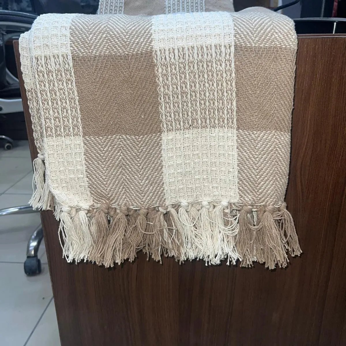 Close view of a beige and white throw with a textured check pattern and fringed edge