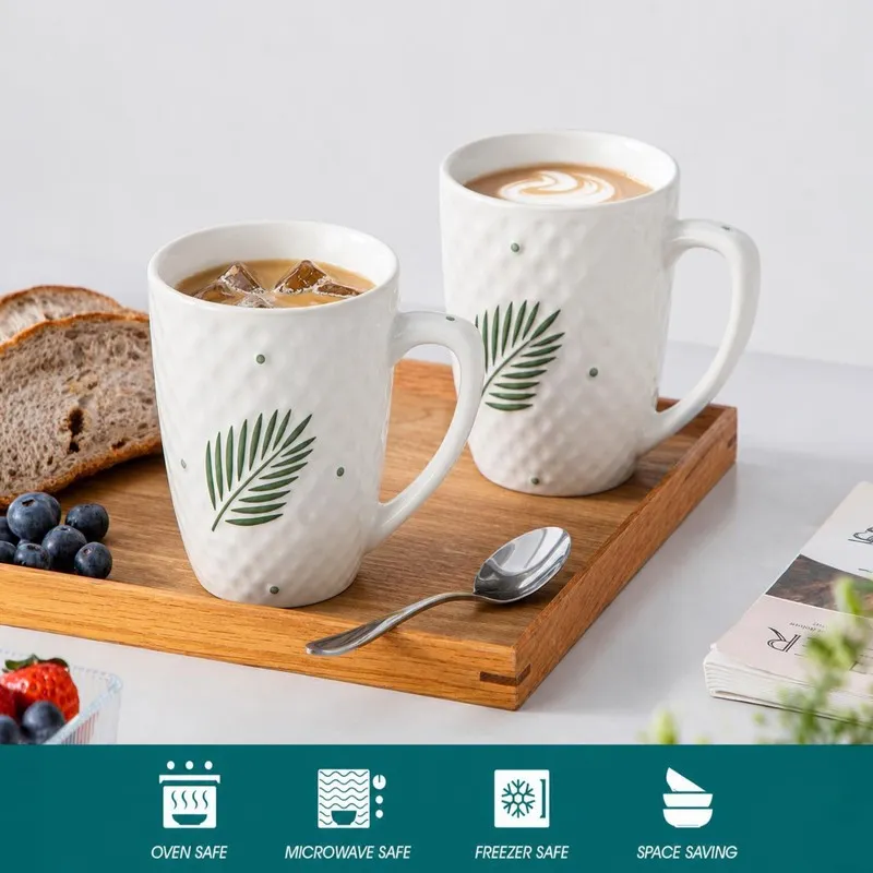 Two white leaf-print mugs with coffee on a wooden serving tray