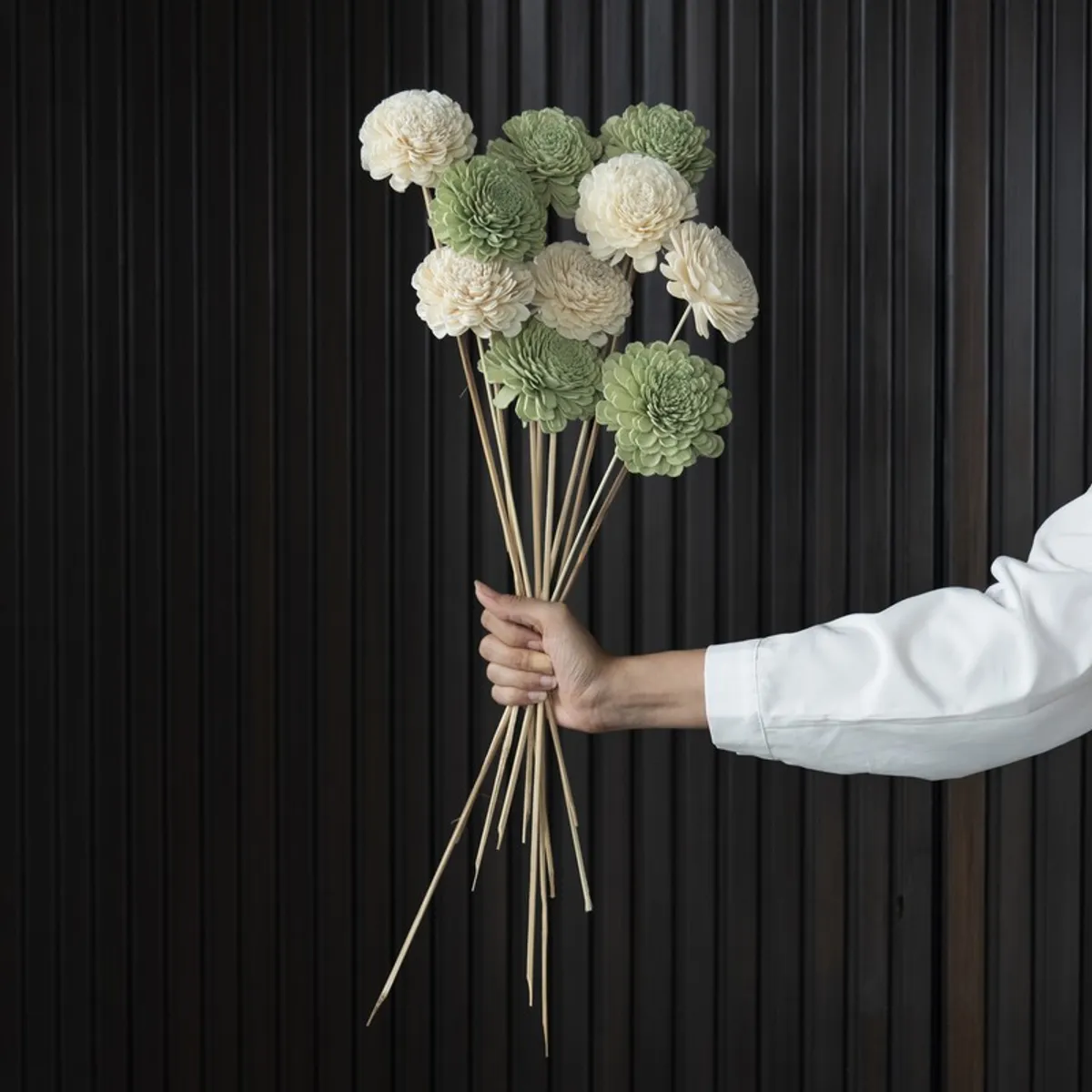 Green and off-white artificial flower sticks held together against a dark panelled backdrop