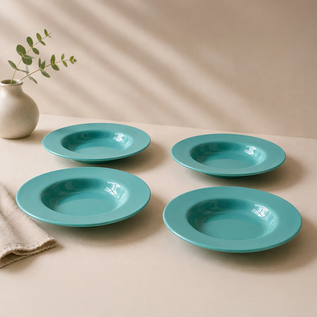 Four teal pasta plates arranged on a dining table