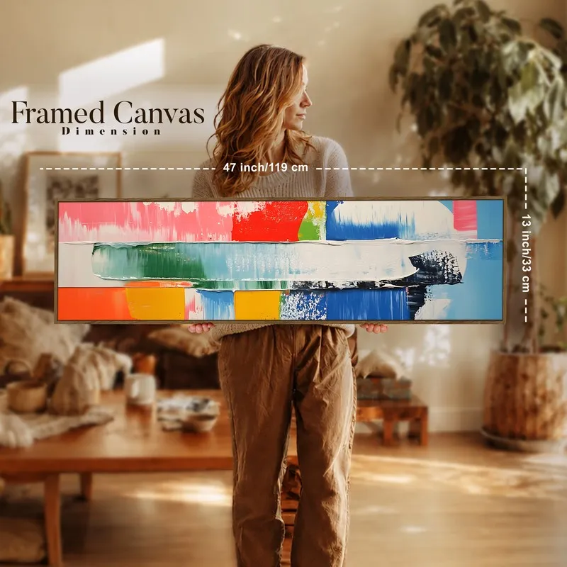 Person holding a long framed abstract canvas artwork in a warm-toned room.