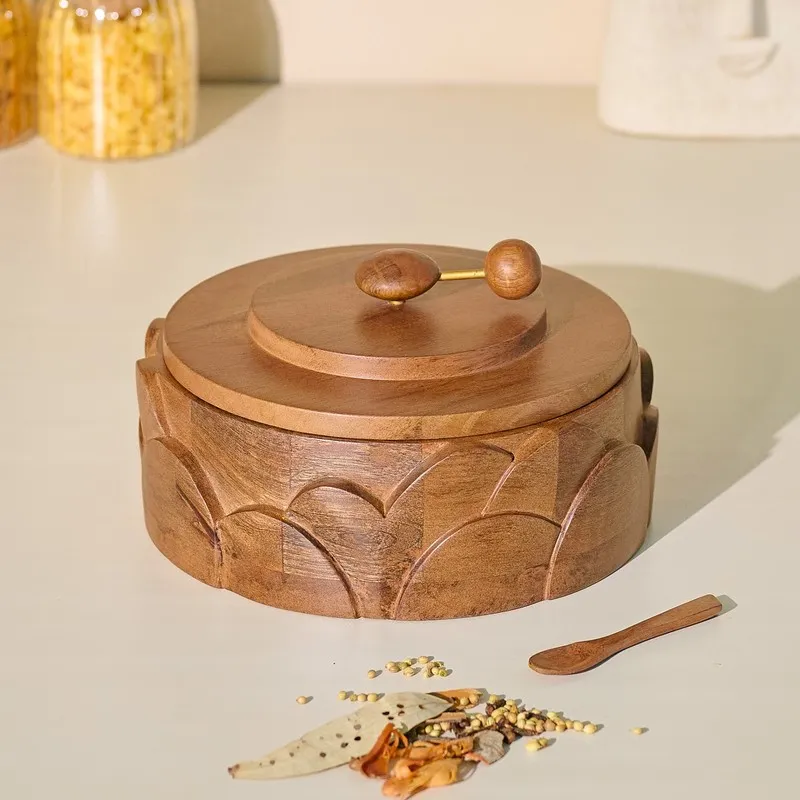 Closed round brown wooden masala box with a rotating metal-pin handle and carved petal-arch detailing.