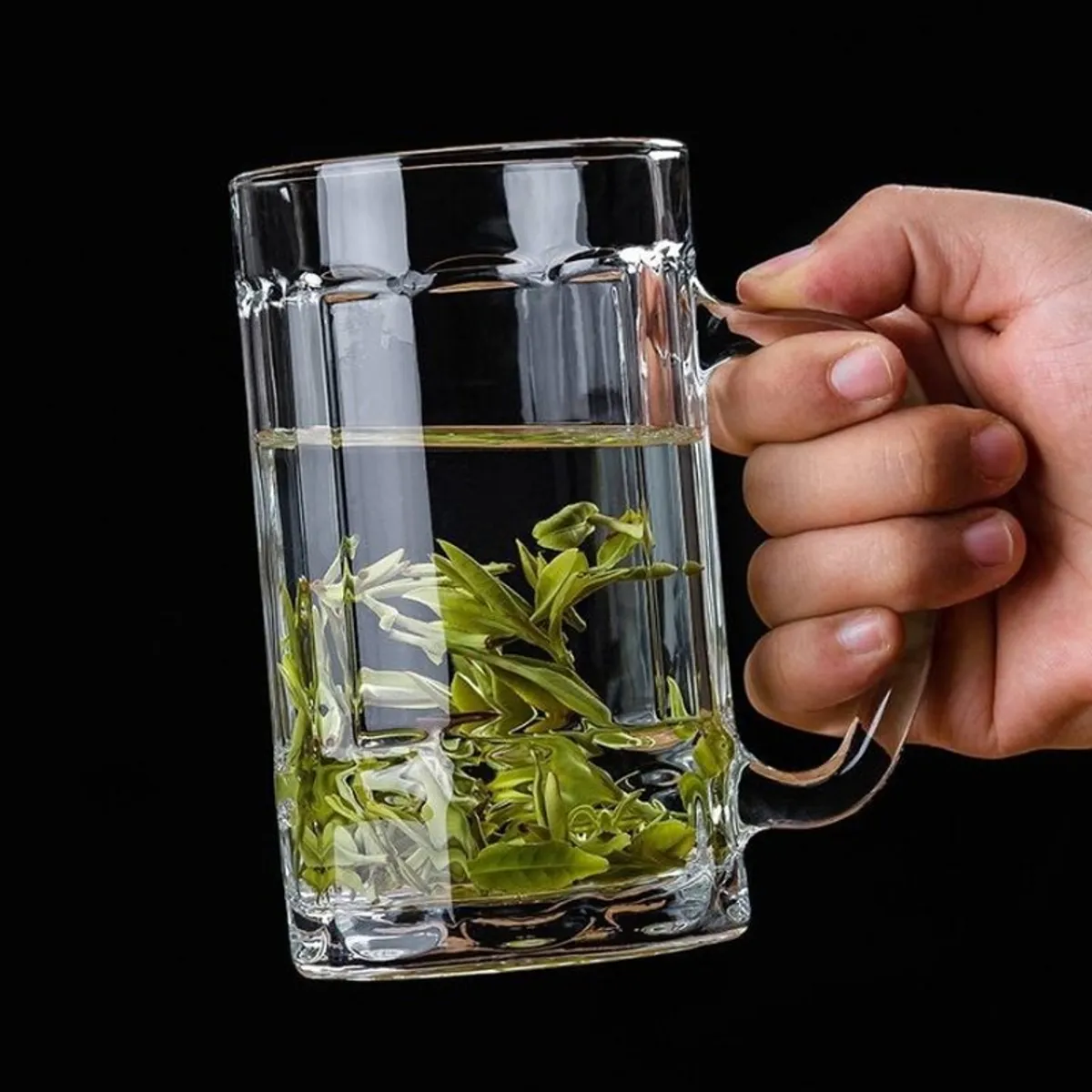 Hand holding a clear glass mug filled with a pale beverage and herbs