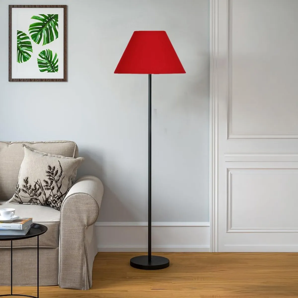 Red floor lamp with a slim black stand placed beside a cream sofa in a bright room.