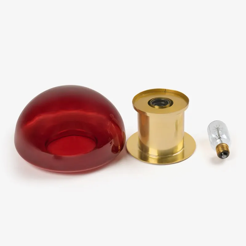 Disassembled red glass shade, gold lamp base and bulb shown together