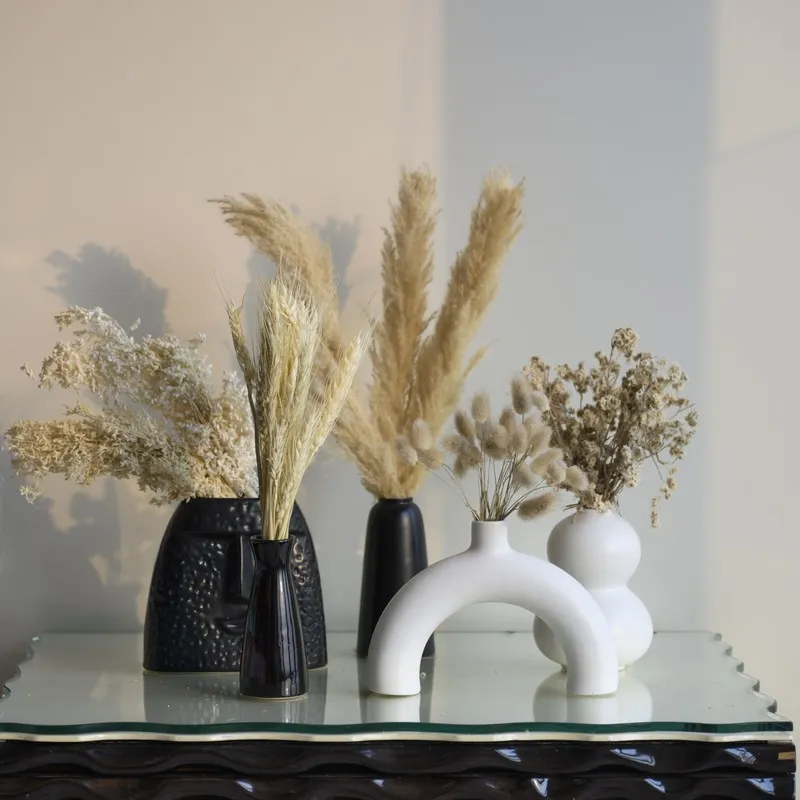 Beige dried flower arrangements styled in contrasting black and white vases.